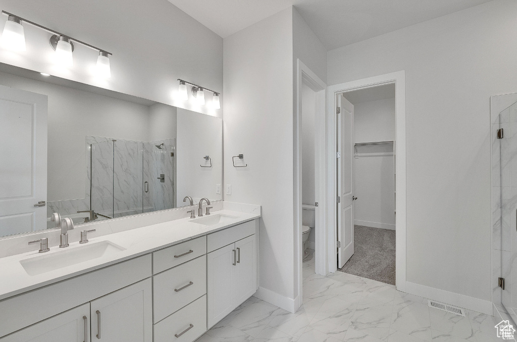 Full bath with a marble finish shower, toilet, double vanity, marble finish flooring, and baseboards