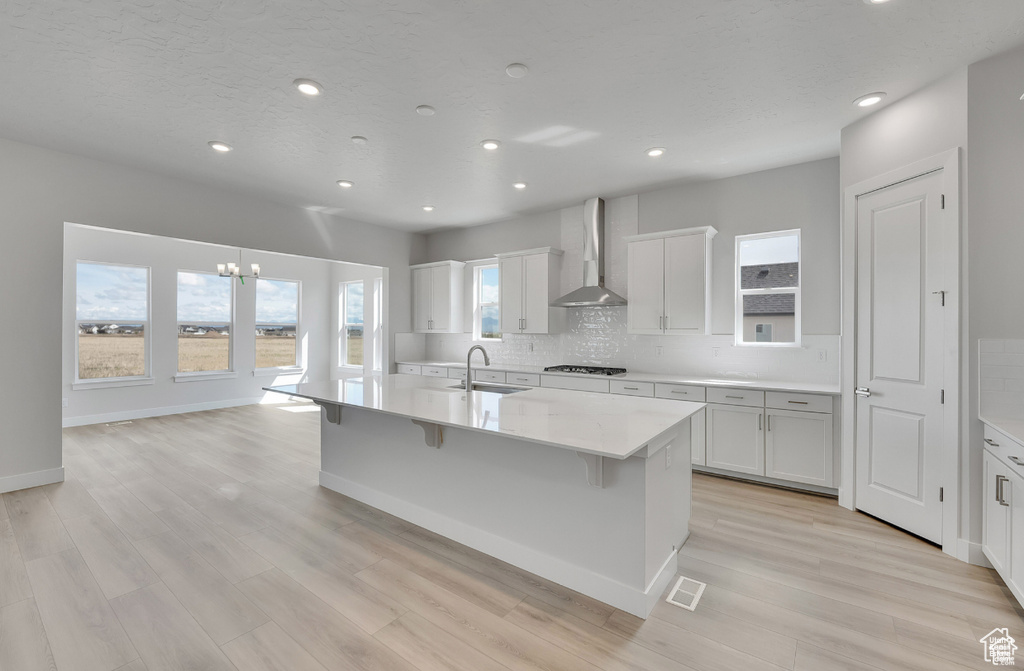 Kitchen featuring wall chimney range hood, gas cooktop, tasteful backsplash, a chandelier, and light countertops