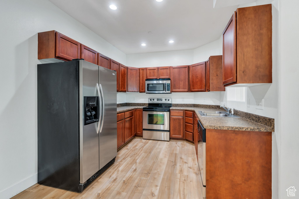 Kitchen with stainless steel appliances, a sink, light wood finished floors, recessed lighting, and dark countertops
