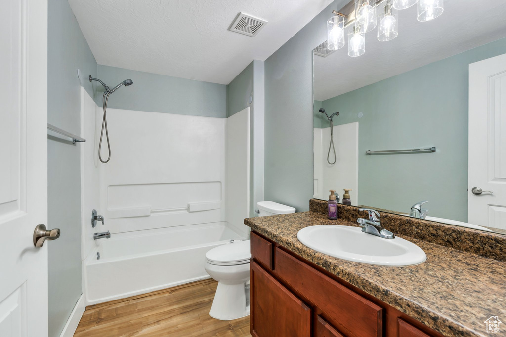 Bathroom featuring wood finished floors, toilet, vanity, and shower / washtub combination