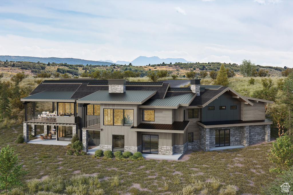Back of property with a chimney, a patio, stone siding, and a balcony