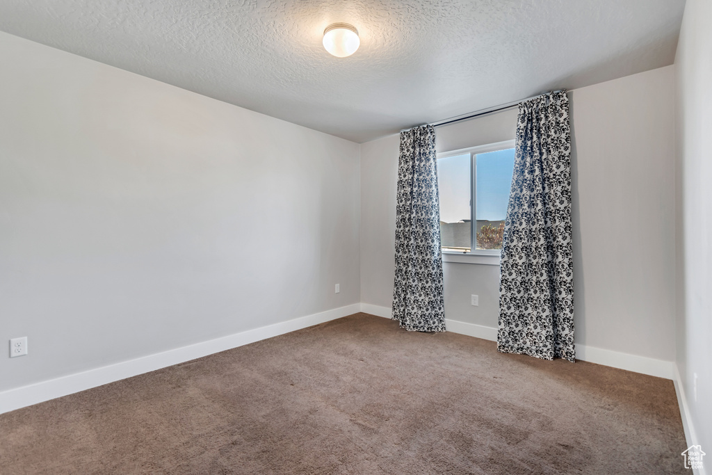 Empty room featuring a textured ceiling, carpet flooring, and baseboards