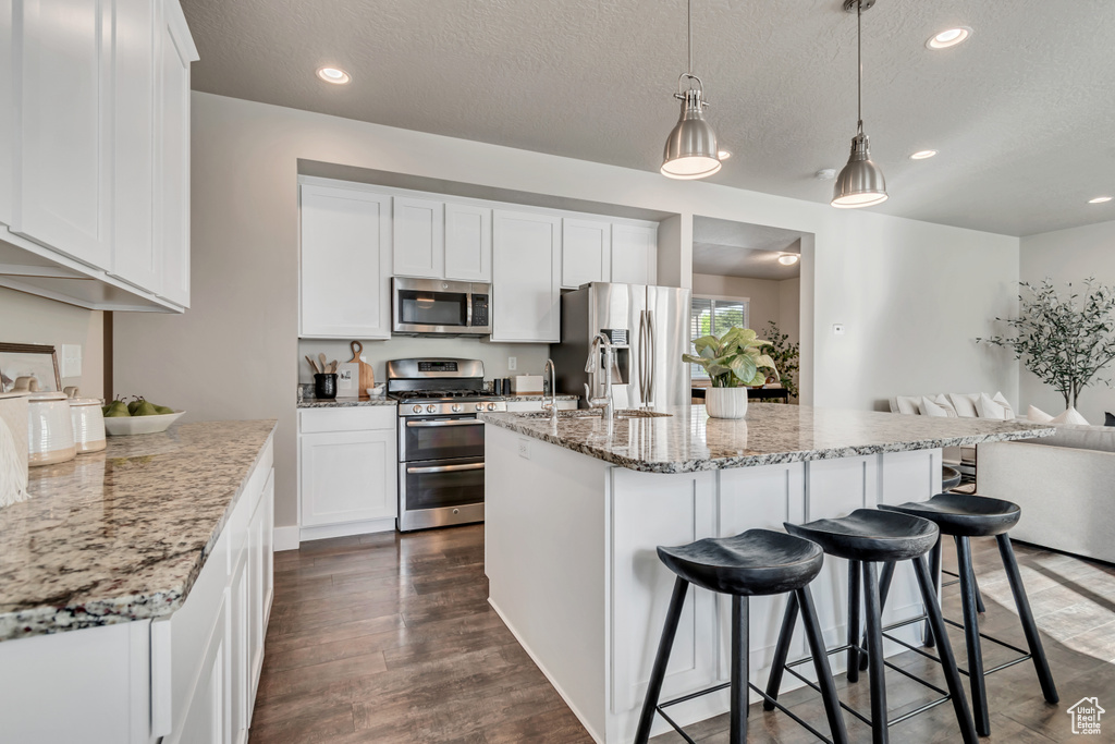 Kitchen with appliances with stainless steel finishes, open floor plan, dark wood-style floors, white cabinets, and a textured ceiling