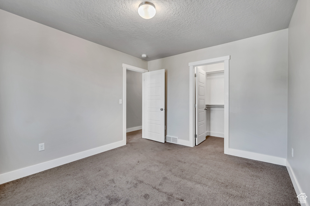 Unfurnished bedroom featuring carpet flooring, baseboards, a textured ceiling, a closet, and a spacious closet