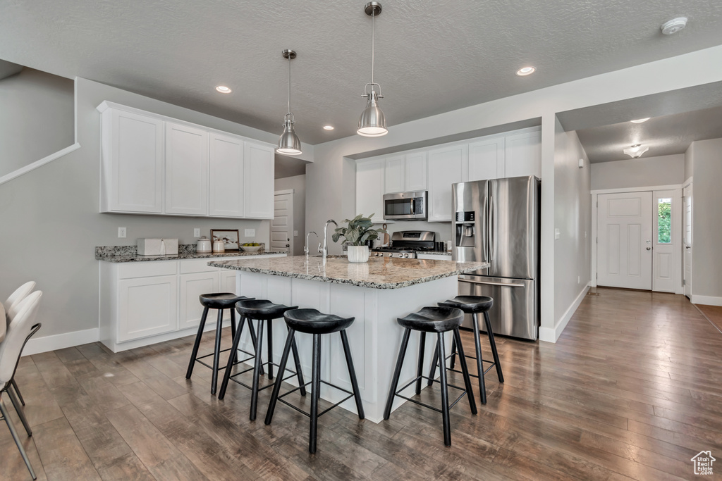 Kitchen with appliances with stainless steel finishes, dark wood finished floors, baseboards, a kitchen breakfast bar, and recessed lighting