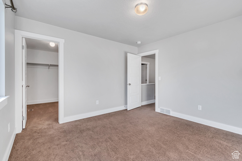 Unfurnished bedroom featuring carpet, a walk in closet, and baseboards