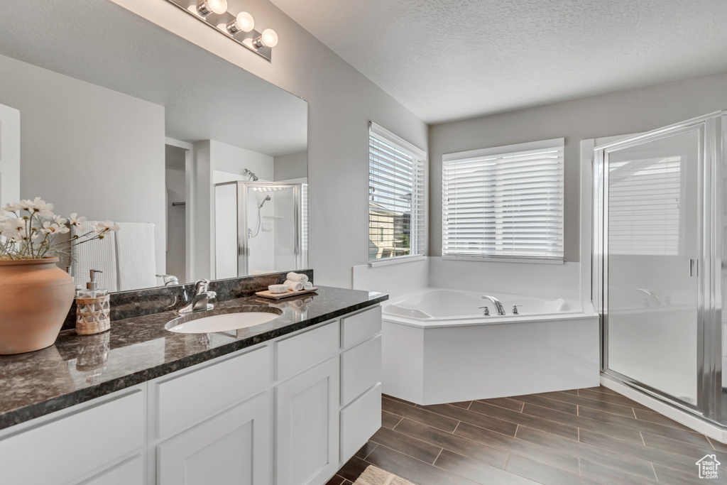 Full bathroom with a stall shower, vanity, a garden tub, a textured ceiling, and wood finished floors