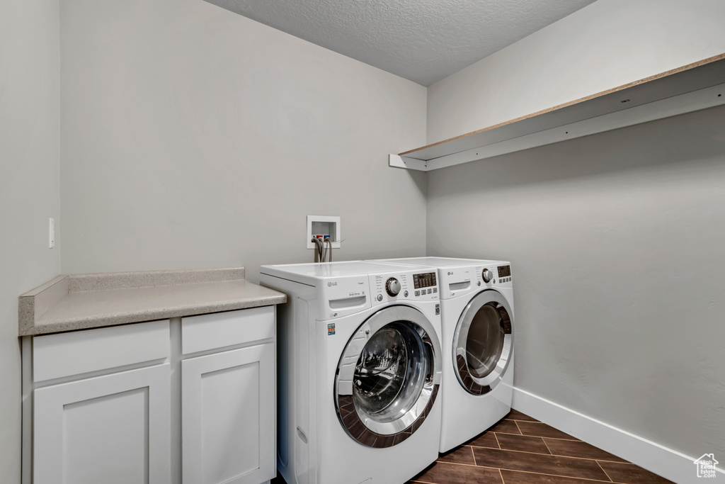 Laundry area with washing machine and clothes dryer, wood tiled floors, a textured ceiling, baseboards, and cabinet space