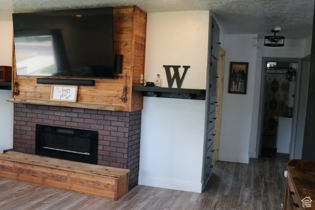 Living room with wood finished floors, a brick fireplace, a textured ceiling, and baseboards