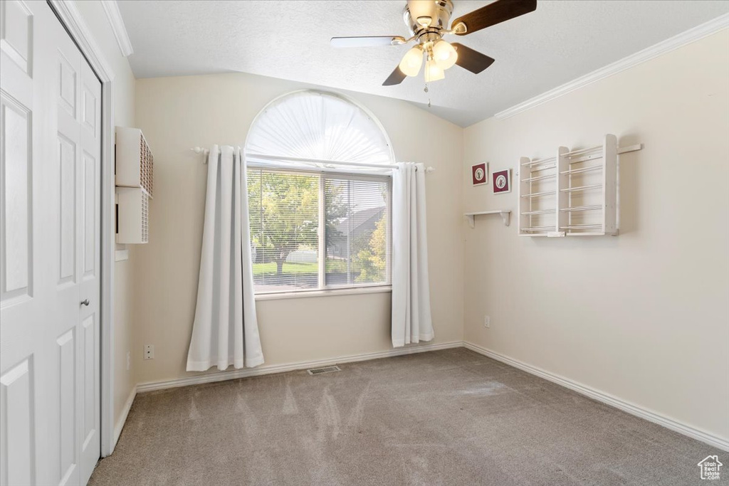 Carpeted spare room featuring a ceiling fan, vaulted ceiling, and baseboards