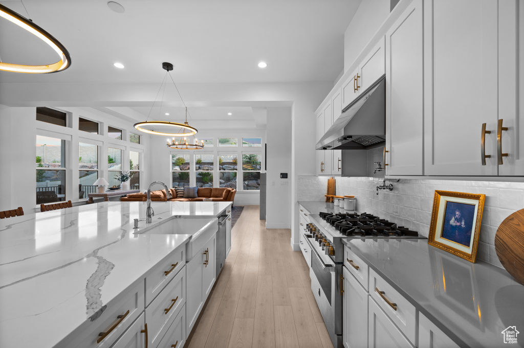 Kitchen with high end stainless steel range, under cabinet range hood, a sink, recessed lighting, and light stone countertops