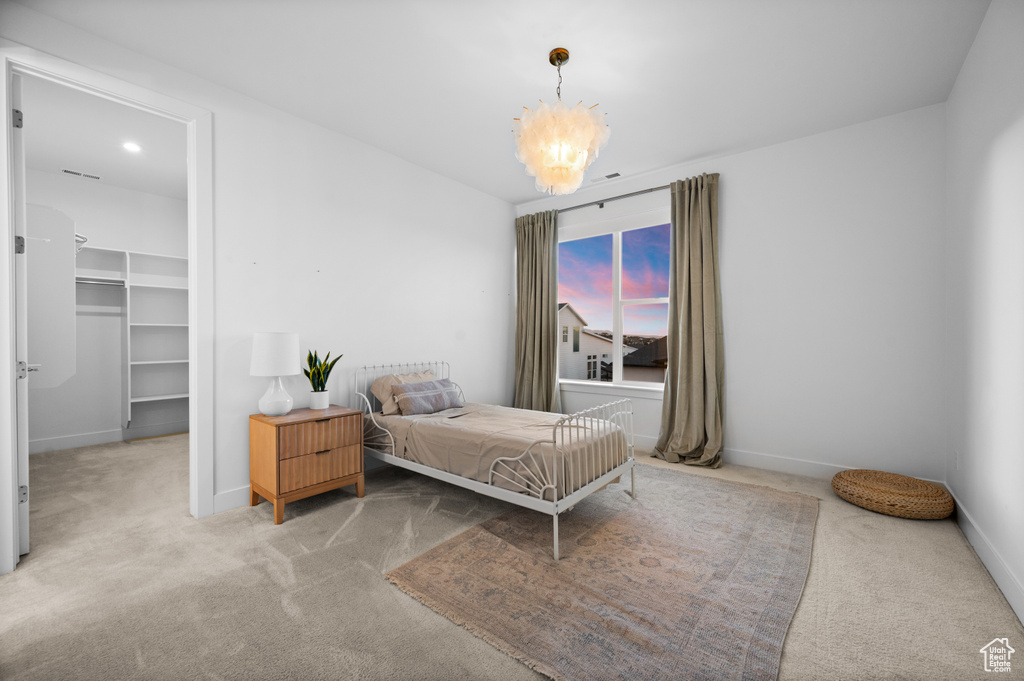 Carpeted bedroom featuring a chandelier, a walk in closet, and baseboards