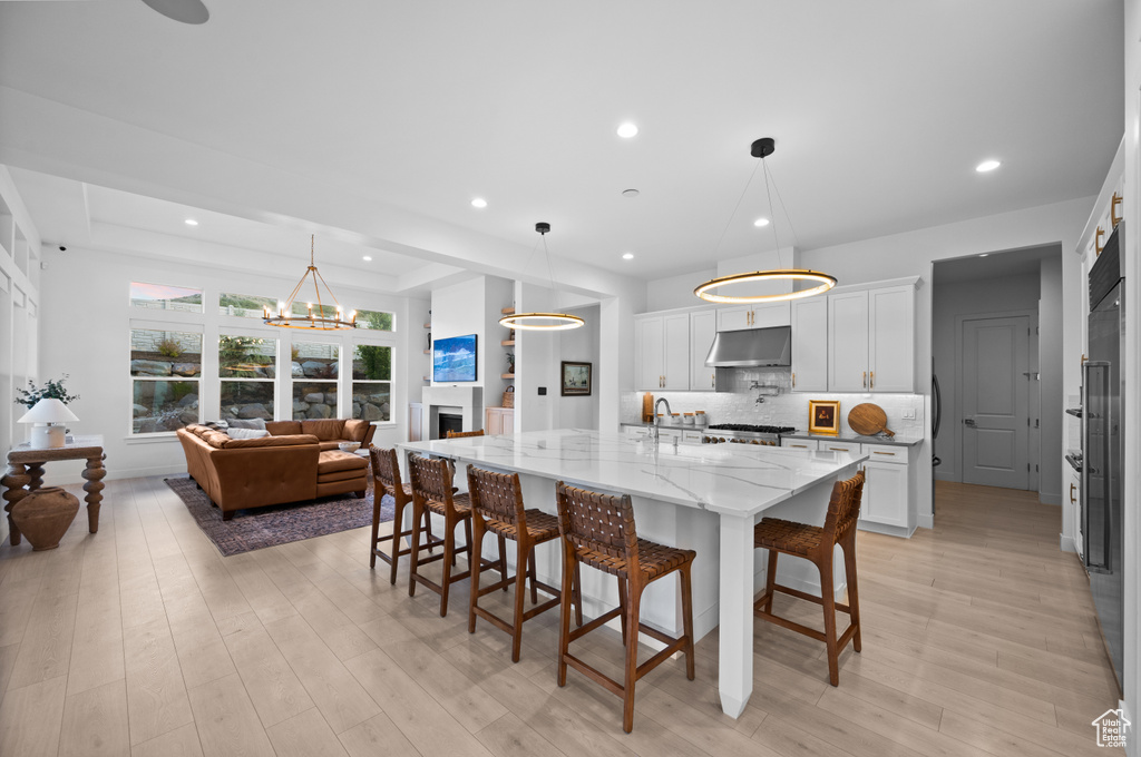Kitchen with under cabinet range hood, a kitchen bar, white cabinets, backsplash, and light stone countertops