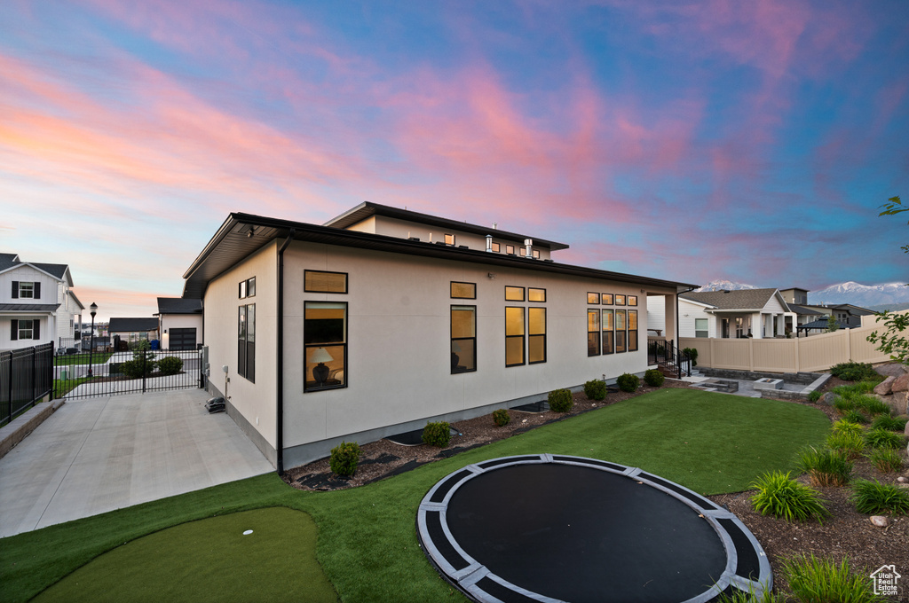 Back of house with a trampoline, a patio, a putting green, and stucco siding