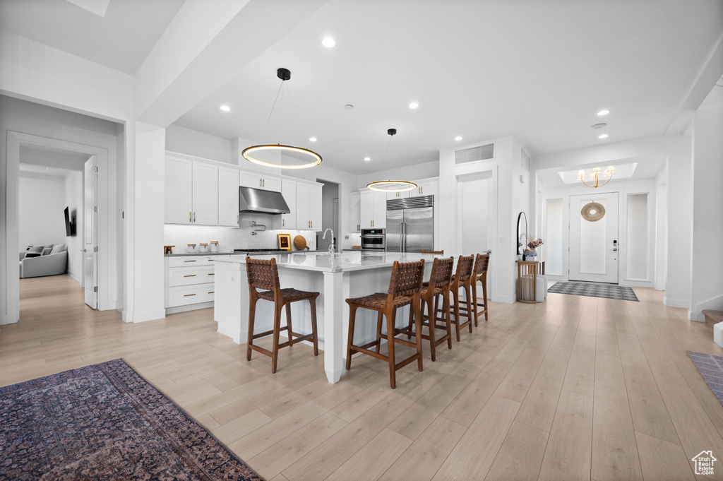 Kitchen featuring stainless steel appliances, under cabinet range hood, a kitchen bar, light countertops, and a chandelier