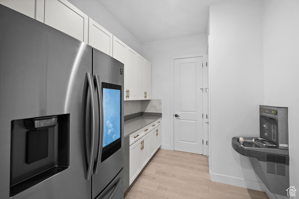 Kitchen featuring stainless steel fridge, light wood-style floors, white cabinets, and baseboards