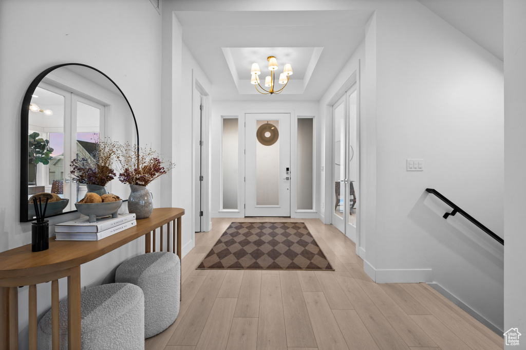 Foyer entrance featuring a chandelier, light wood finished floors, baseboards, and a tray ceiling
