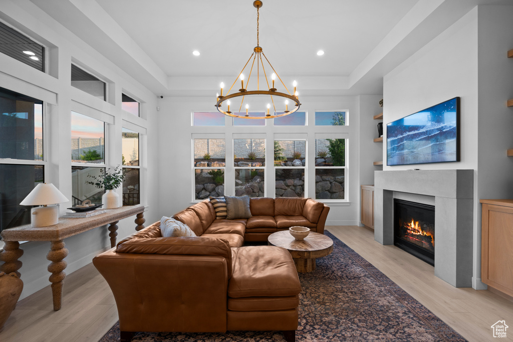 Living area with a tray ceiling, a glass covered fireplace, plenty of natural light, light wood-type flooring, and recessed lighting