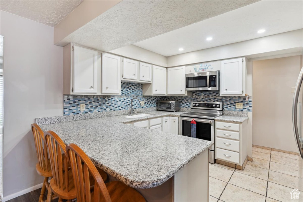 Kitchen featuring appliances with stainless steel finishes, a sink, a peninsula, a kitchen breakfast bar, and white cabinets