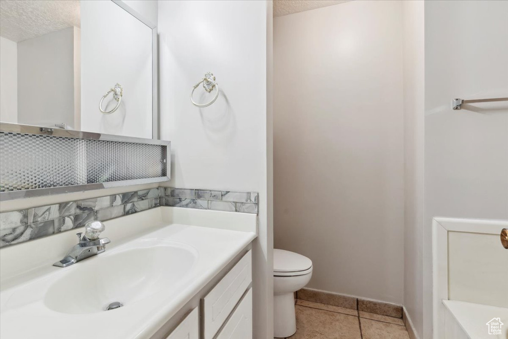 Bathroom featuring toilet, tile patterned floors, vanity, a textured ceiling, and baseboards