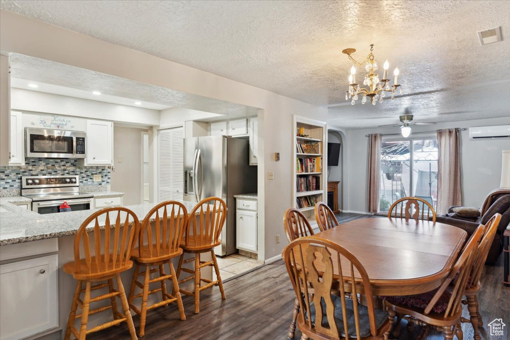 Dining space featuring a wall mounted AC, a textured ceiling, a ceiling fan, light wood finished floors, and a chandelier