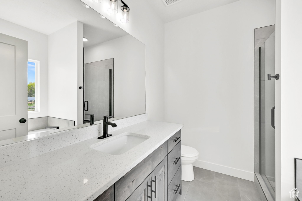 Bathroom featuring vanity, a stall shower, tile patterned floors, toilet, and baseboards