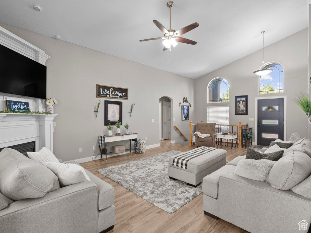 Living room featuring high vaulted ceiling, ceiling fan, arched walkways, light wood-type flooring, and a fireplace
