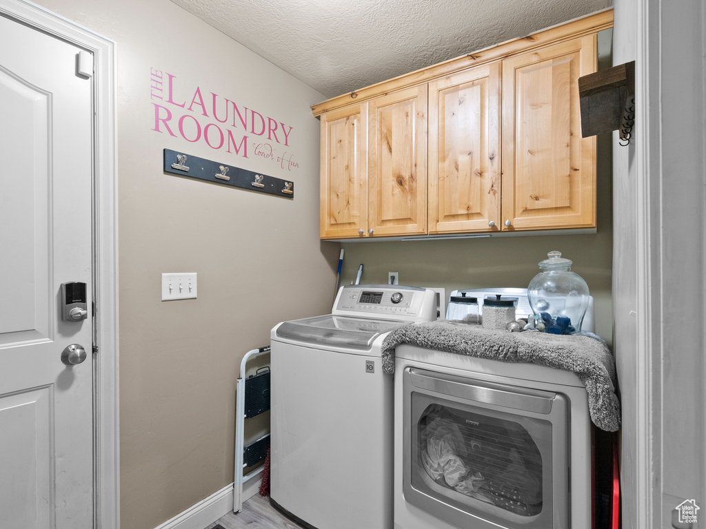 Laundry room with cabinet space, washing machine and dryer, a textured ceiling, and wood finished floors