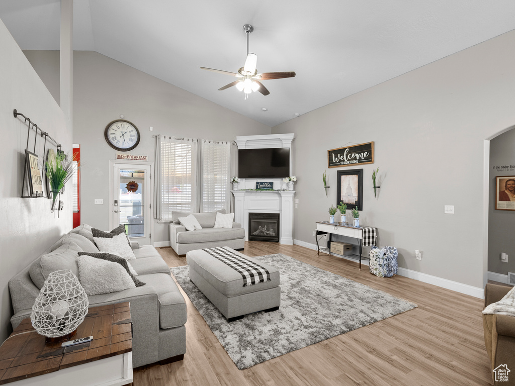 Living area featuring a ceiling fan, a glass covered fireplace, wood finished floors, baseboards, and high vaulted ceiling