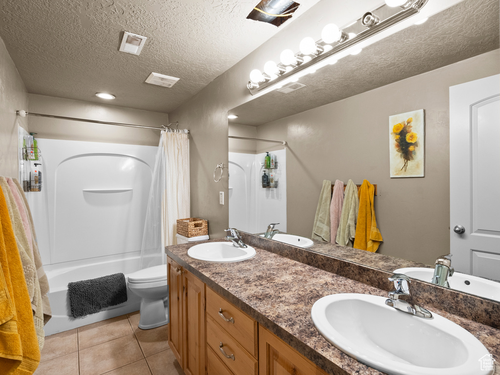Full bath featuring double vanity, toilet, shower / bathtub combination with curtain, tile patterned flooring, and a textured ceiling