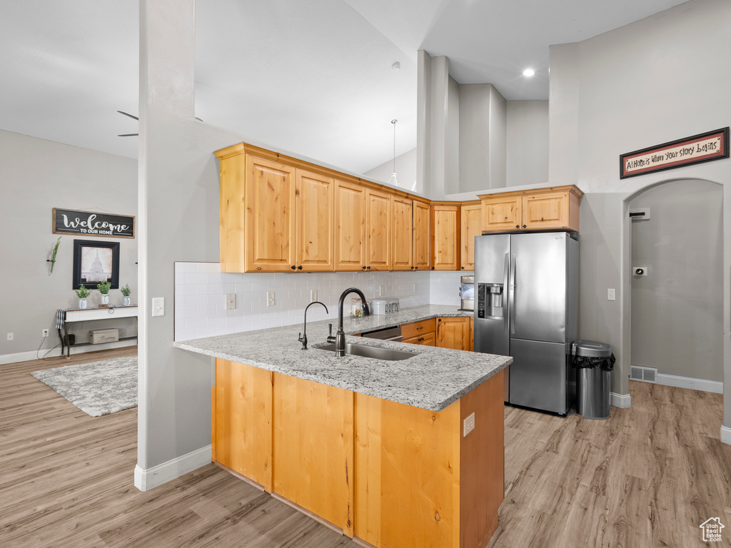 Kitchen featuring stainless steel fridge with ice dispenser, a sink, a peninsula, baseboards, and light stone counters