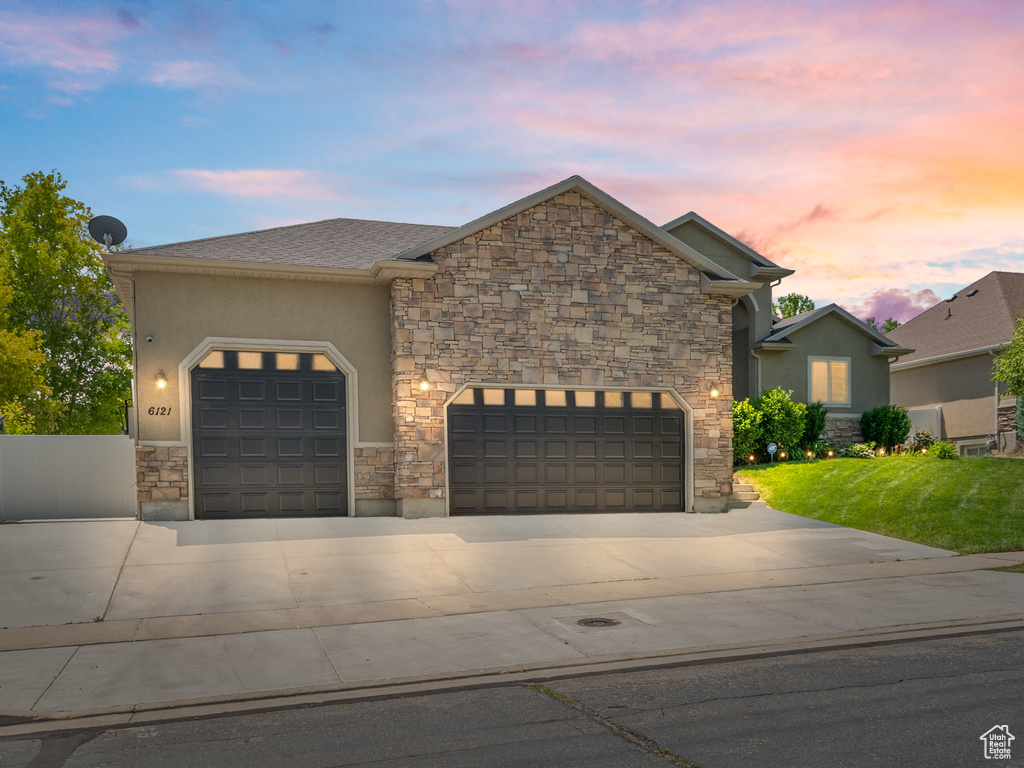 View of front of home featuring concrete driveway, an attached garage, stone siding, stucco siding, and a front yard