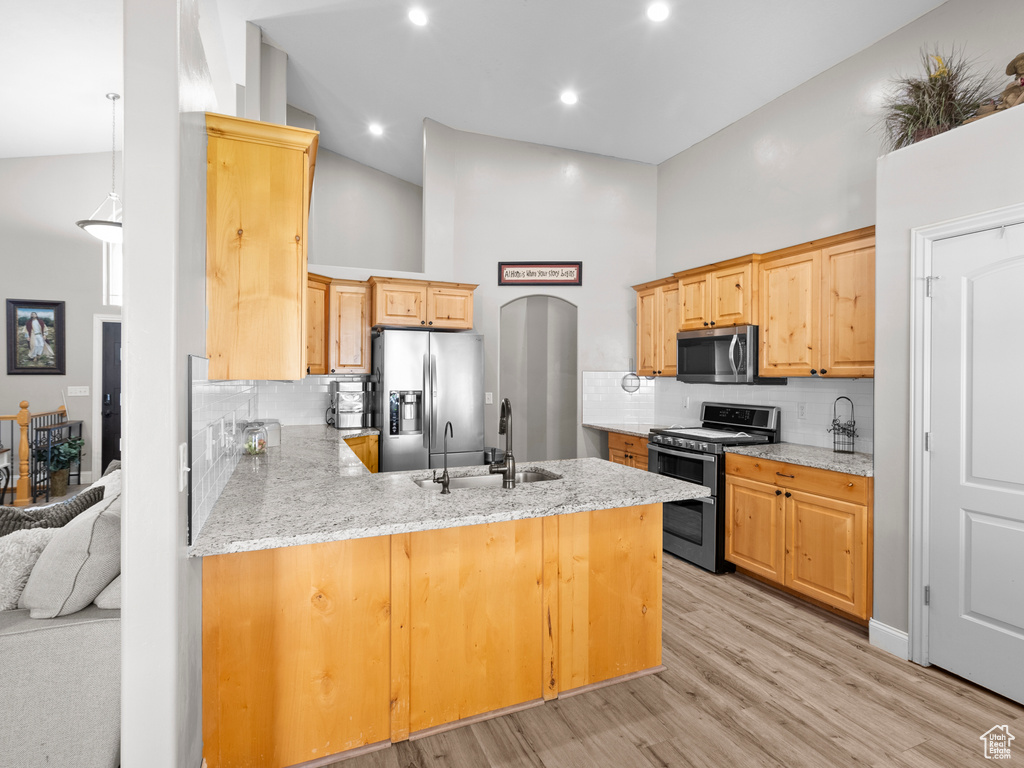 Kitchen with appliances with stainless steel finishes, a towering ceiling, a peninsula, tasteful backsplash, and light wood-type flooring