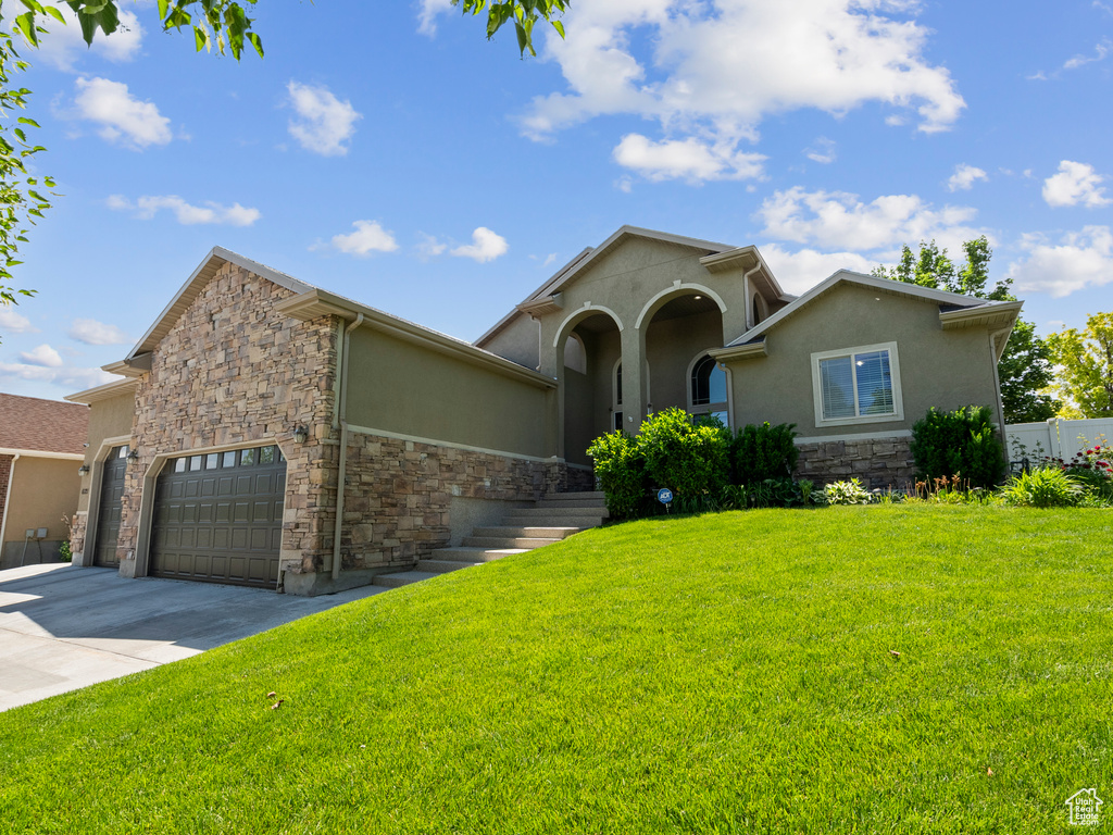 Mediterranean / spanish house featuring stone siding, stucco siding, concrete driveway, and a front lawn
