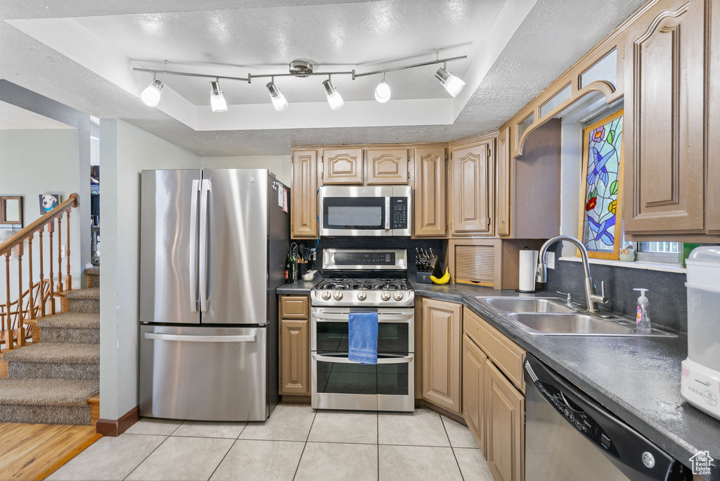 Kitchen with appliances with stainless steel finishes, a sink, dark countertops, a textured ceiling, and tasteful backsplash