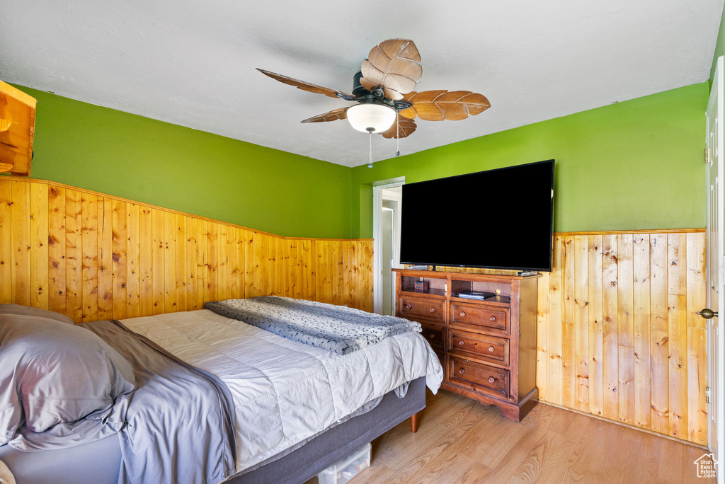 Bedroom with wainscoting, wood walls, wood finished floors, and a ceiling fan