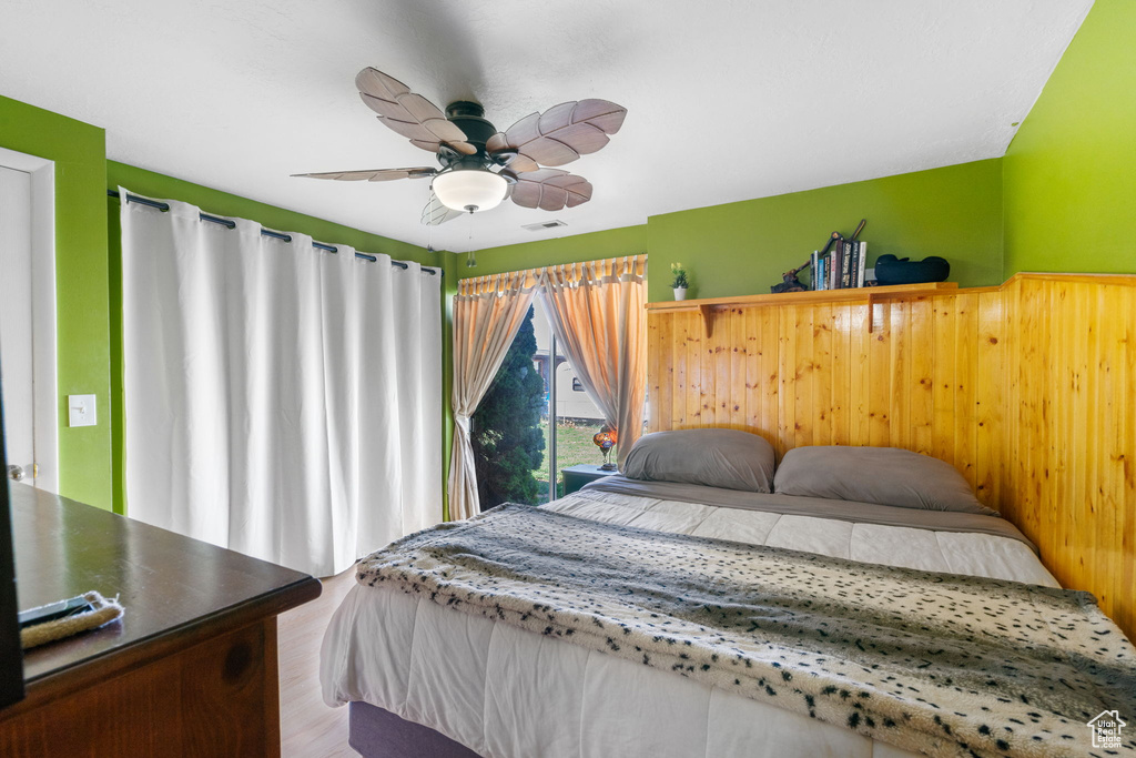Bedroom featuring a ceiling fan, wood finished floors, and wooden walls