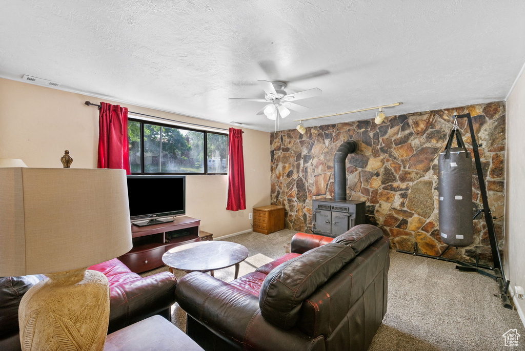 Living area featuring a wood stove, track lighting, carpet, ceiling fan, and a textured ceiling
