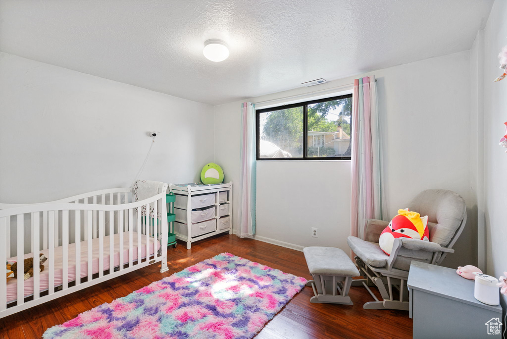 Bedroom with wood finished floors, a crib, a textured ceiling, and baseboards