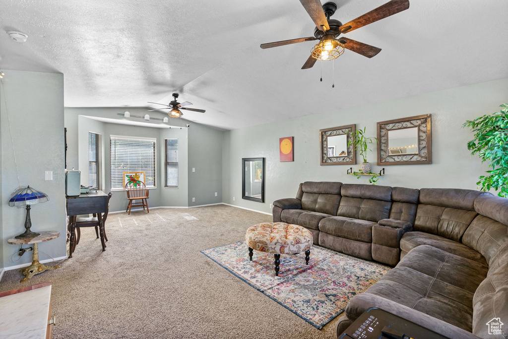 Living area featuring ceiling fan, light carpet, vaulted ceiling, baseboards, and a textured ceiling