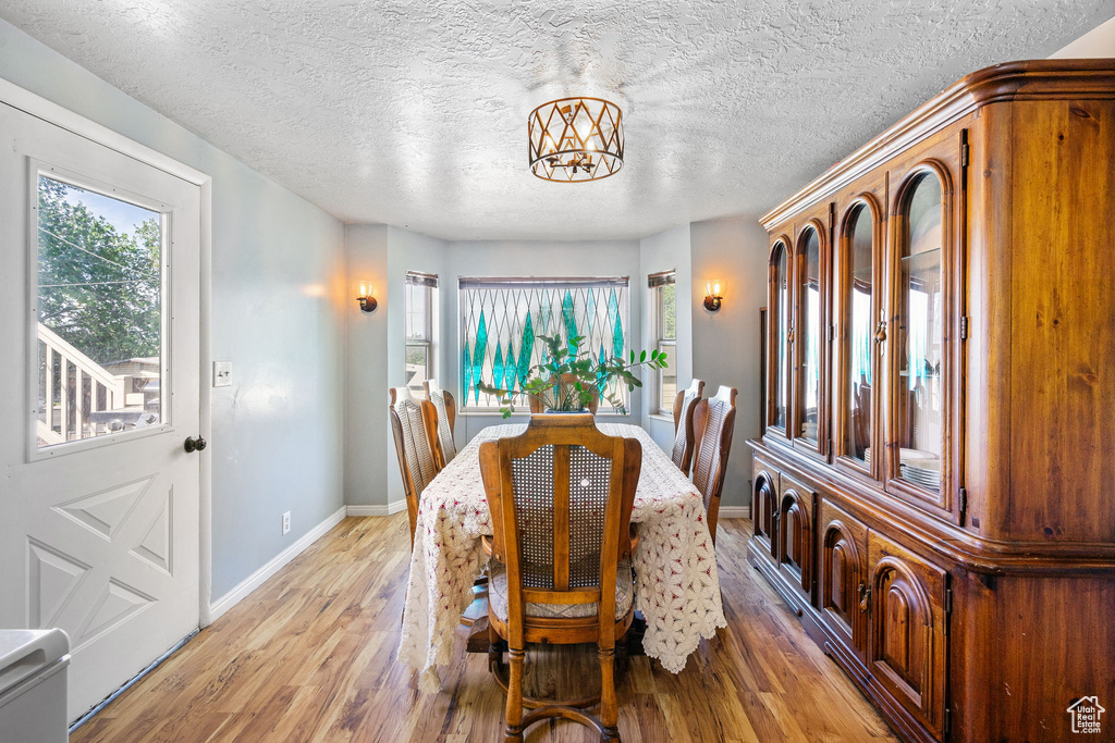 Dining room featuring a chandelier, baseboards, light wood-type flooring, and a textured ceiling