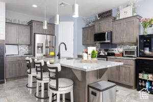 Kitchen featuring stainless steel appliances, a kitchen breakfast bar, decorative light fixtures, backsplash, and a kitchen island with sink