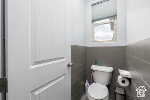 Bathroom with toilet, a wainscoted wall, and tile walls