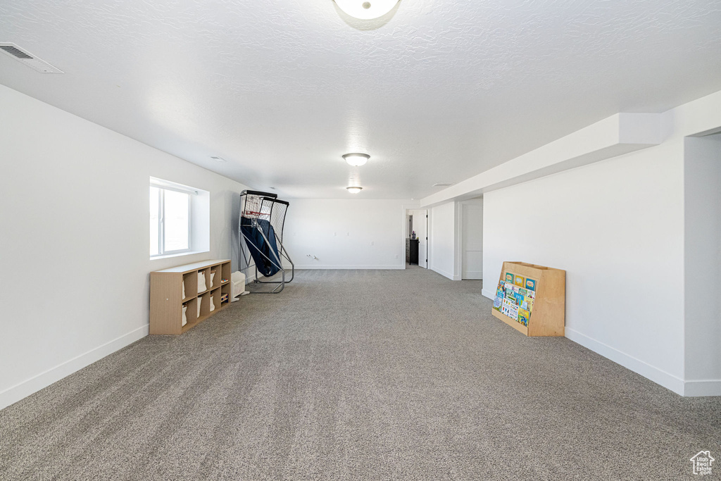Basement featuring baseboards, light colored carpet, and a textured ceiling