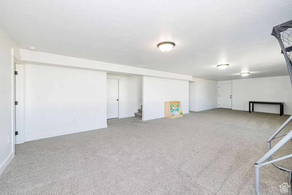 Finished below grade area with carpet flooring, stairway, baseboards, and a textured ceiling