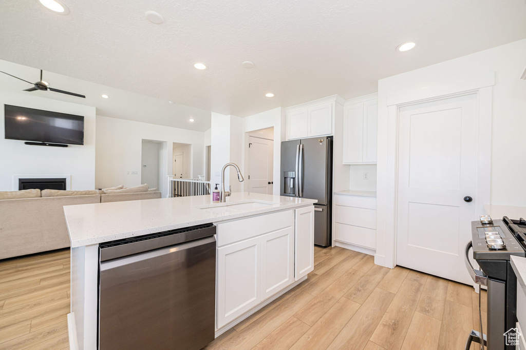 Kitchen featuring stainless steel appliances, a sink, open floor plan, light wood-style floors, and white cabinets