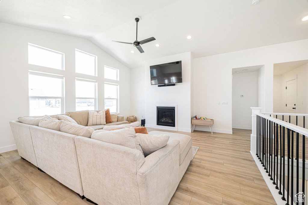 Living area featuring ceiling fan, light wood finished floors, a glass covered fireplace, baseboards, and high vaulted ceiling