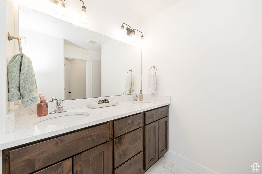 Full bath featuring double vanity, marble finish floors, and baseboards