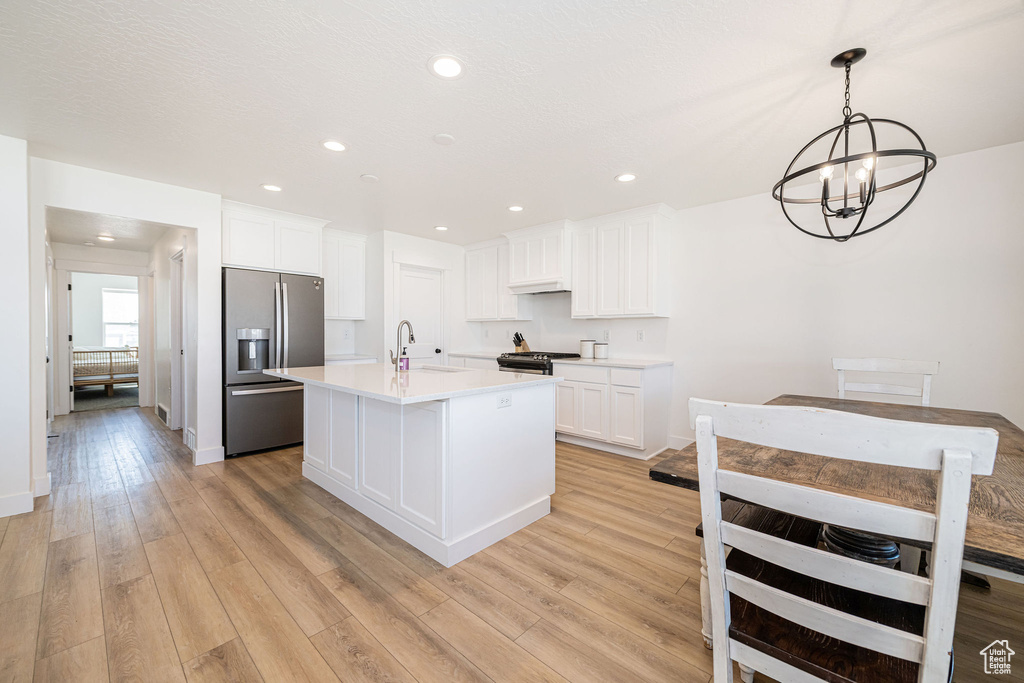 Kitchen with stainless steel appliances, a sink, a chandelier, light wood-style floors, and white cabinetry