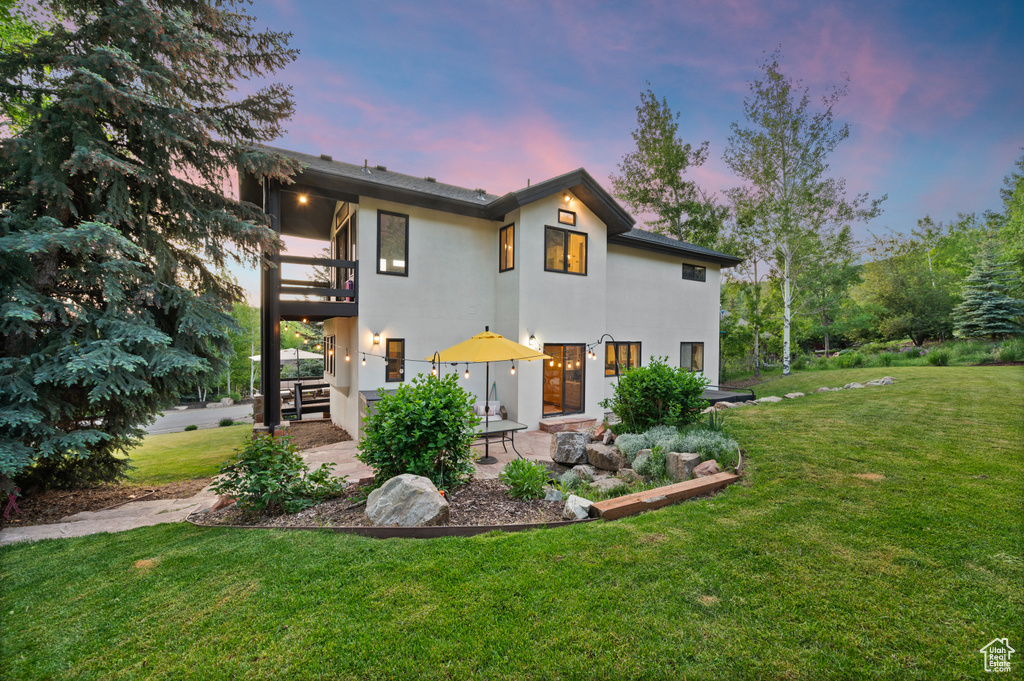 Contemporary house with stucco siding, a lawn, a patio area, and a balcony